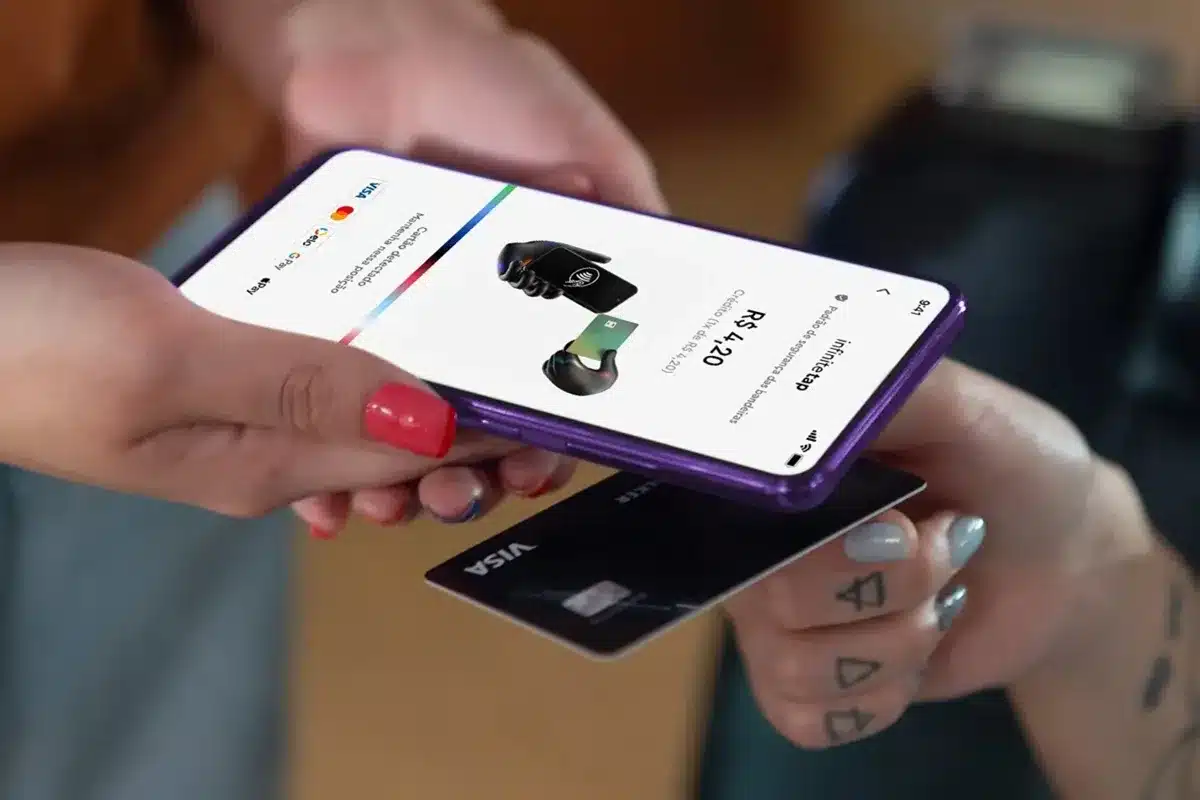 Pessoa realizando pagamento por aproximação com smartphone roxo, exibindo interface de transação, e cartão Visa sendo utilizado no processo