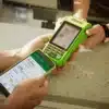 Máquina de cartão Stone verde sendo utilizada junto a um smartphone exibindo dados financeiros em um balcão, representando tecnologia e eficiência em pagamentos.