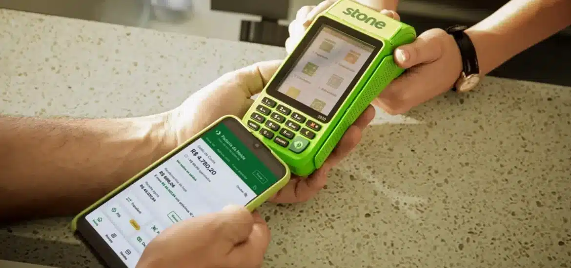 Máquina de cartão Stone verde sendo utilizada junto a um smartphone exibindo dados financeiros em um balcão, representando tecnologia e eficiência em pagamentos.