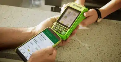 Máquina de cartão Stone verde sendo utilizada junto a um smartphone exibindo dados financeiros em um balcão, representando tecnologia e eficiência em pagamentos.