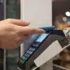 Pessoa usando smartphone azul para realizar pagamento por aproximação em uma máquina de cartão moderna, destacando conveniência e tecnologia contactless