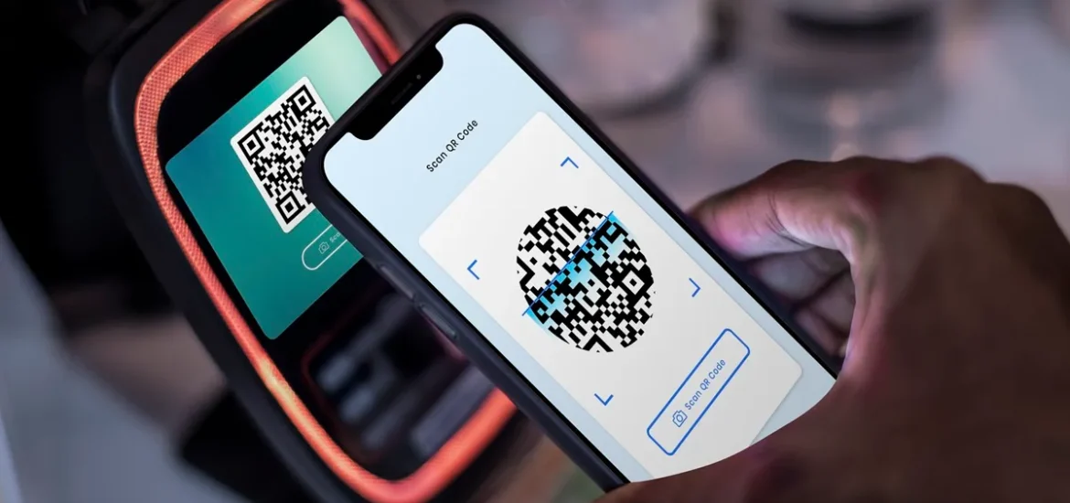 Pessoa usando um smartphone para escanear um código QR em uma máquina de pagamento digital iluminada.