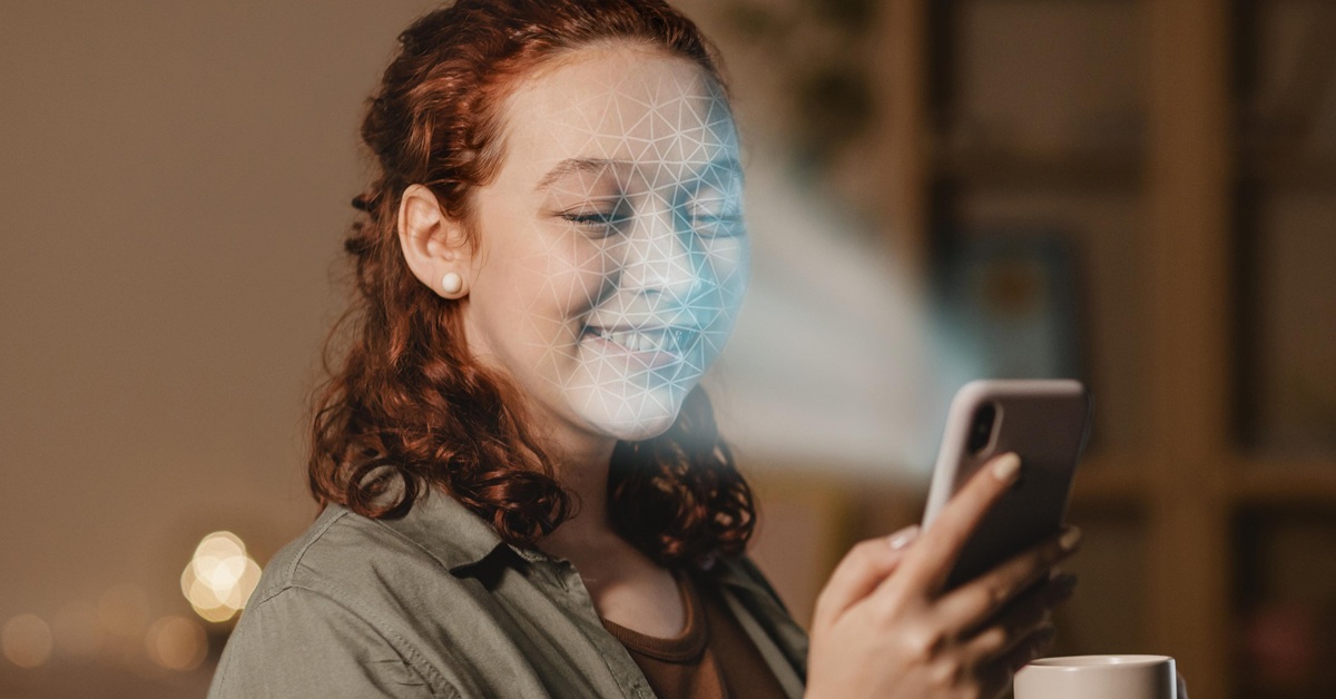 Mulher sorrindo enquanto utiliza reconhecimento facial em um smartphone, com luz azul projetada em seu rosto, representando tecnologia de Inteligência Artificial.