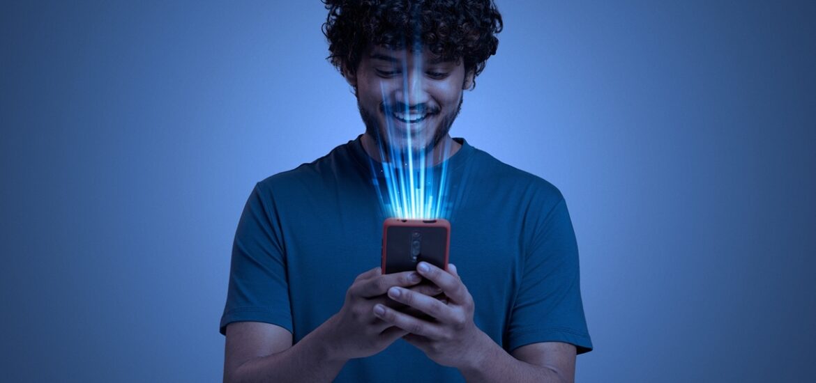 Homem sorrindo enquanto utiliza um smartphone com feixes de luz azul representando tecnologia avançada e inteligência artificial.