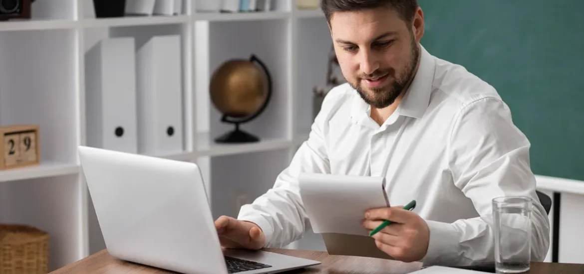 Homem analisando documentos com laptop em ambiente de trabalho organizado.