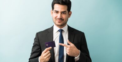 Homem de terno segurando e apontando para um cartão de crédito, com fundo azul claro.