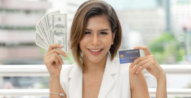 Mulher sorridente segurando notas de dólar e cartão de crédito, simbolizando transações financeiras no exterior e facilidade em pagamentos internacionais