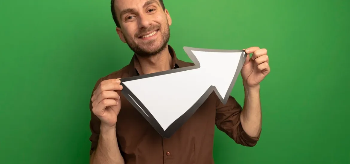 Homem sorridente segurando uma seta branca apontada para cima em um fundo verde.