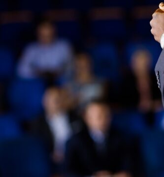 Pessoa em um púlpito falando para uma plateia em auditório, representando discussões sobre o limite de faturamento do MEI no Congresso