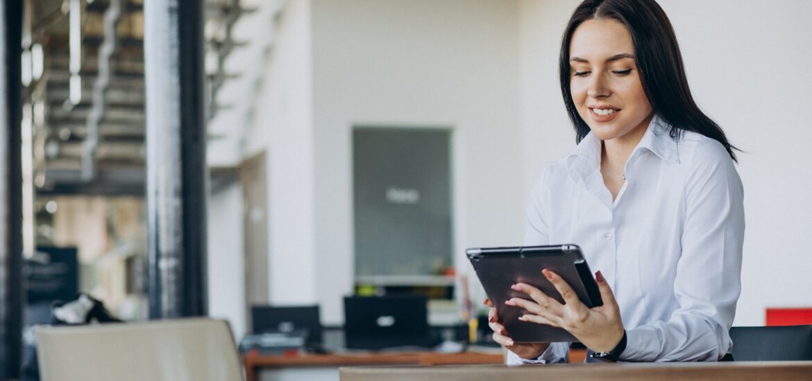 Mulher de negócios sorrindo enquanto faz split de pagamentos e analisa informações em um tablet em um ambiente de escritório moderno.