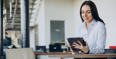 Mulher de negócios sorrindo enquanto faz split de pagamentos e analisa informações em um tablet em um ambiente de escritório moderno.