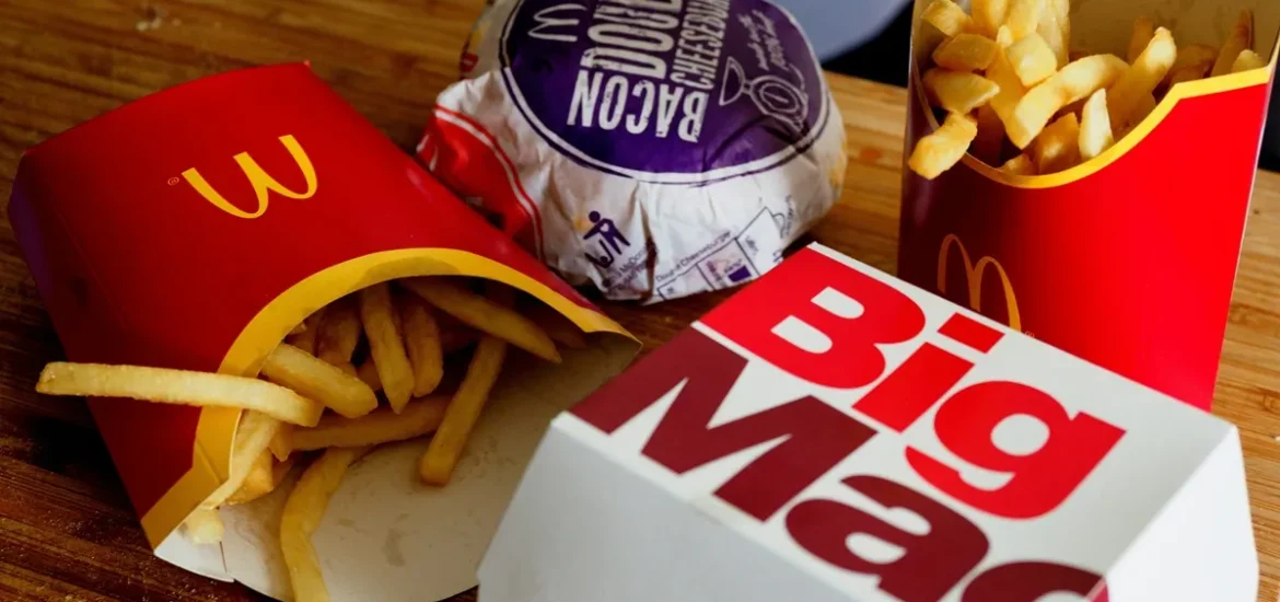  Combo do McDonald's com batatas fritas, hambúrguer Double Bacon Cheeseburger e Big Mac sobre uma tábua de madeira, representando refeição de fast food.